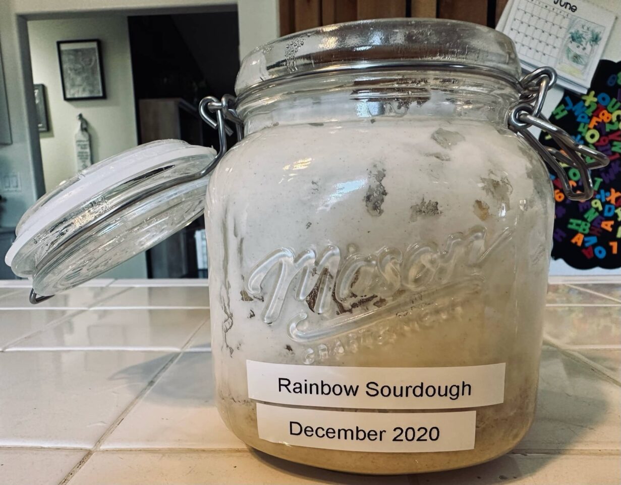 A clear glass mason jar of sourdough starter titled "Rainbow Sourdough, December 2020" is in Sue Evergreen's kitchen.