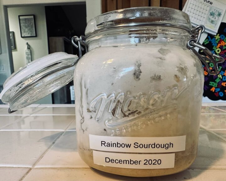 A clear glass mason jar of sourdough starter titled "Rainbow Sourdough, December 2020" is in Sue Evergreen's kitchen.