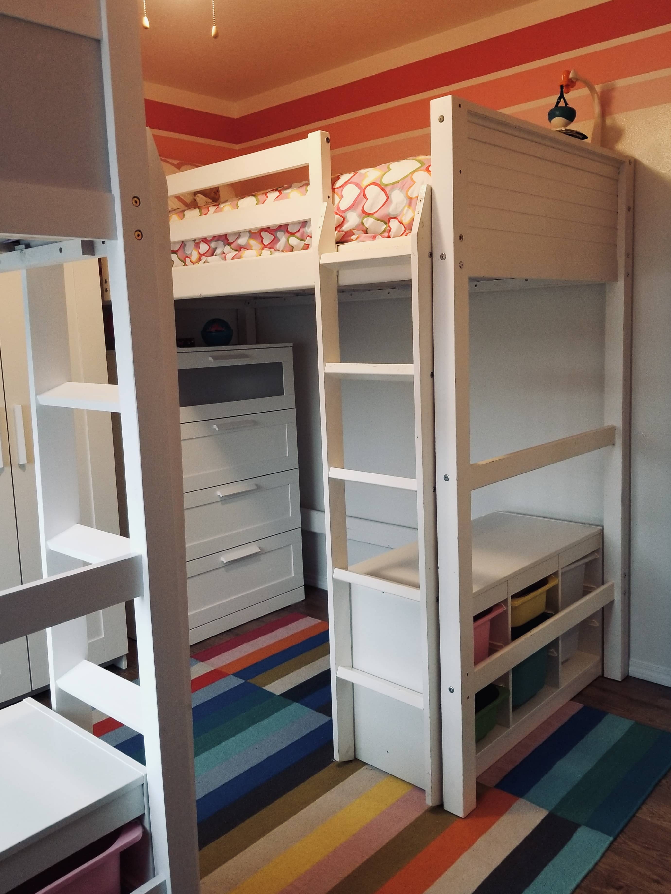 finished laminate flooring in a small kids room with pink striped paint white bunk beds and furniture and a multicolor rug