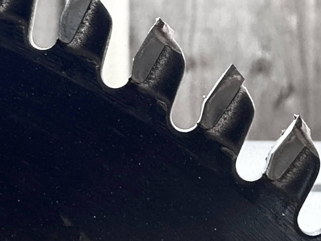 Black and white close-up image of a Duwalt 10-inch table saw blade's teeth and a curved expansion slot.