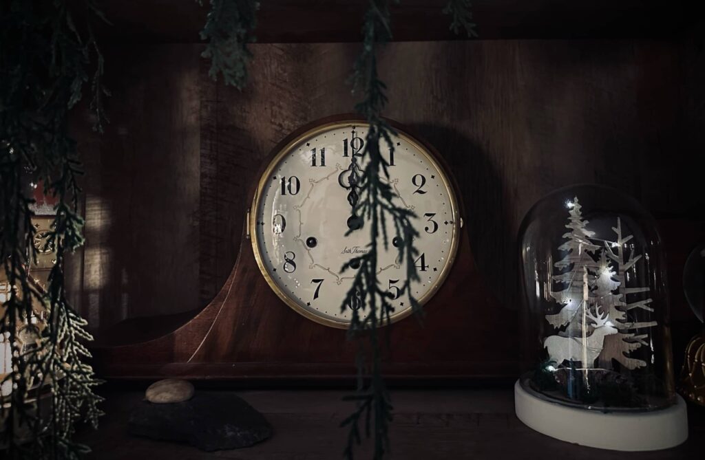 An antique clock surrounded by glass lit up holiday globes and posted in Making Room for Precious Stones by Sue Evergreen on Dropping Rocks.