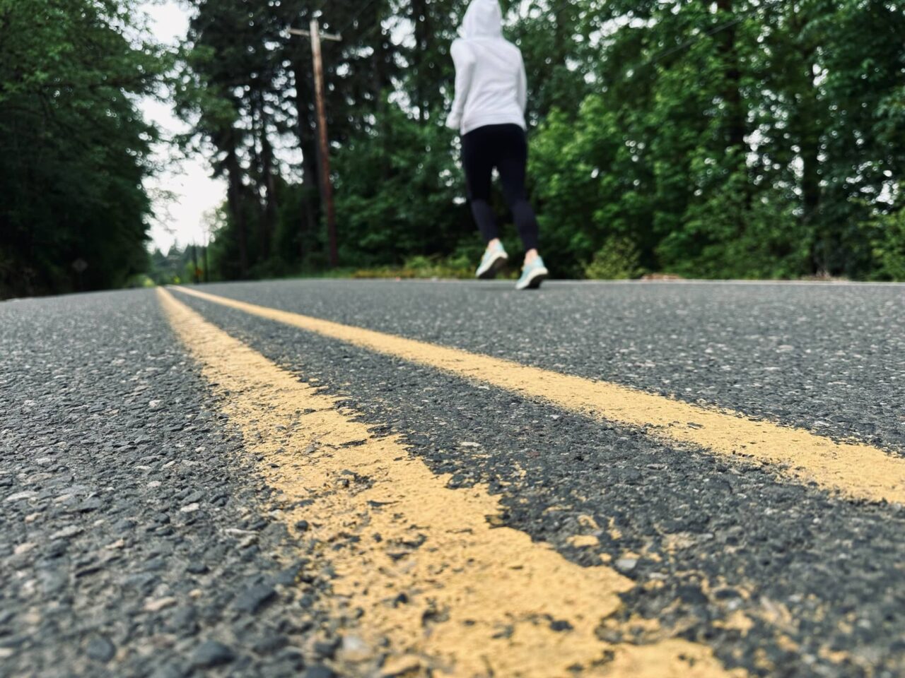 Sue is running down a road with trees all around. Posted in Why Do I Need To Run a Marathon on Dropping Rocks.