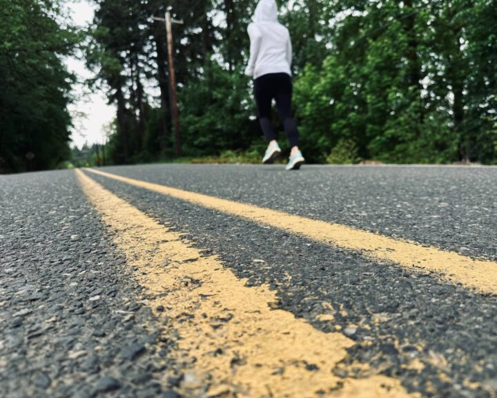 Sue is running down a road with trees all around. Posted in Why Do I Need To Run a Marathon on Dropping Rocks.