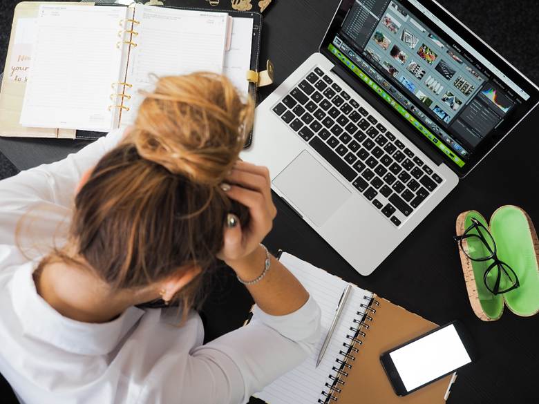 A burnt-out, stressed-out woman in front of her workload of notebooks and a laptop.